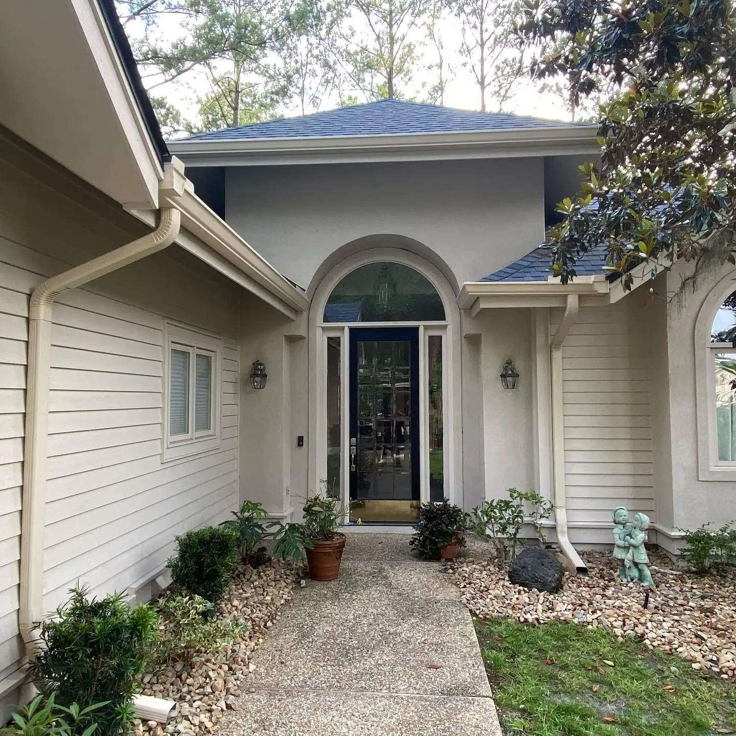 Arched front entry of a tan home with gutters and downspouts. Gutter services in Palmetto Bluff, SC by A&A Island Services