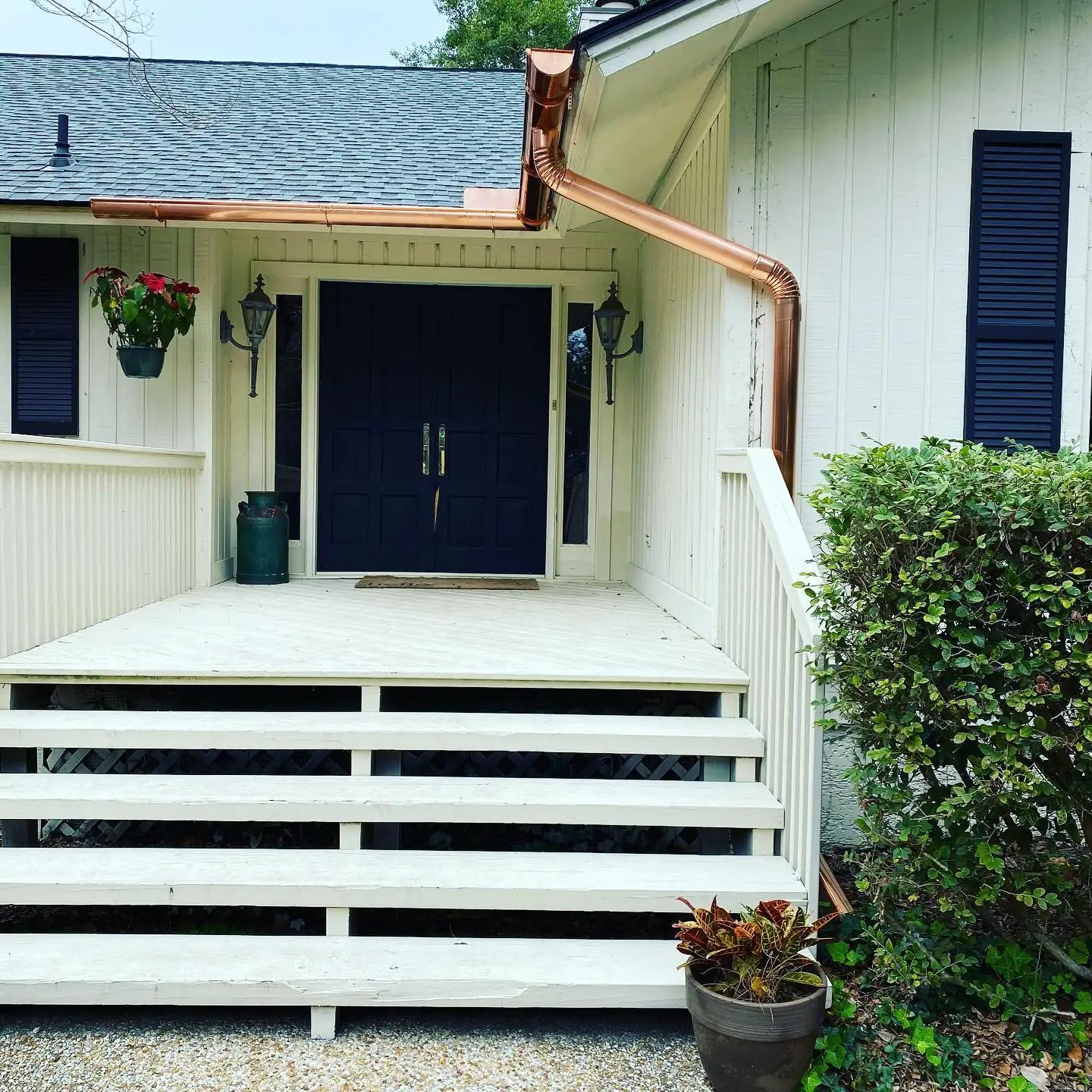 Copper gutter and copper downspout over the front entry of a white home with navy double doors. Gutter cleaning and gutter installation in Bluffton, SC by A&A Island Services