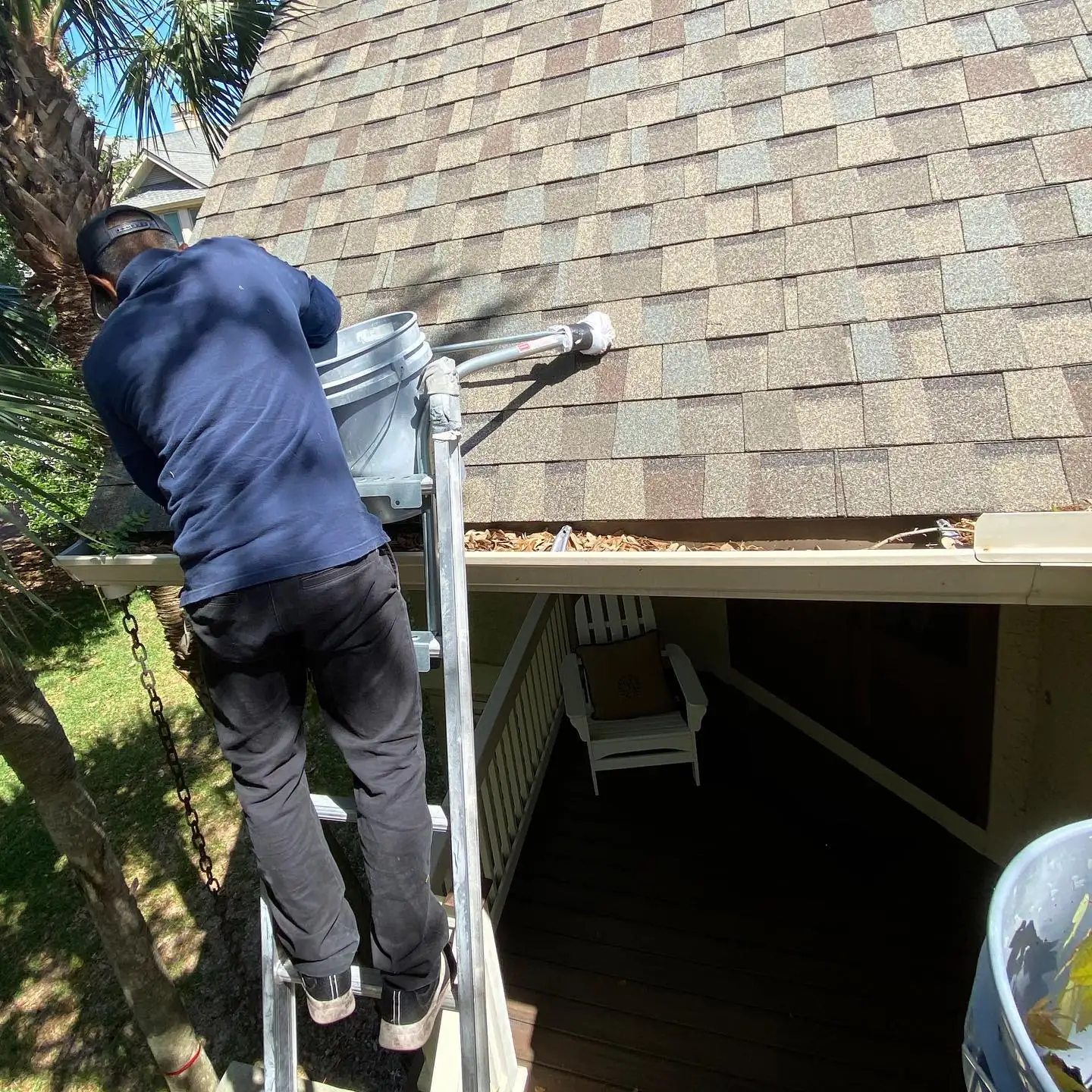 A&A crew member on a ladder clearing leaves and pine needles from a gutter into a bucket. Gutter cleaning and gutter installation in Bluffton, SC by A&A Island Services