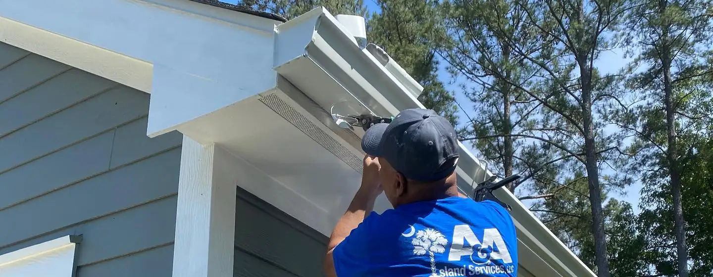 A&A crew member fastening a white gutter under the eave. Gutter cleaning and gutter installation in Bluffton, SC by A&A Island Services