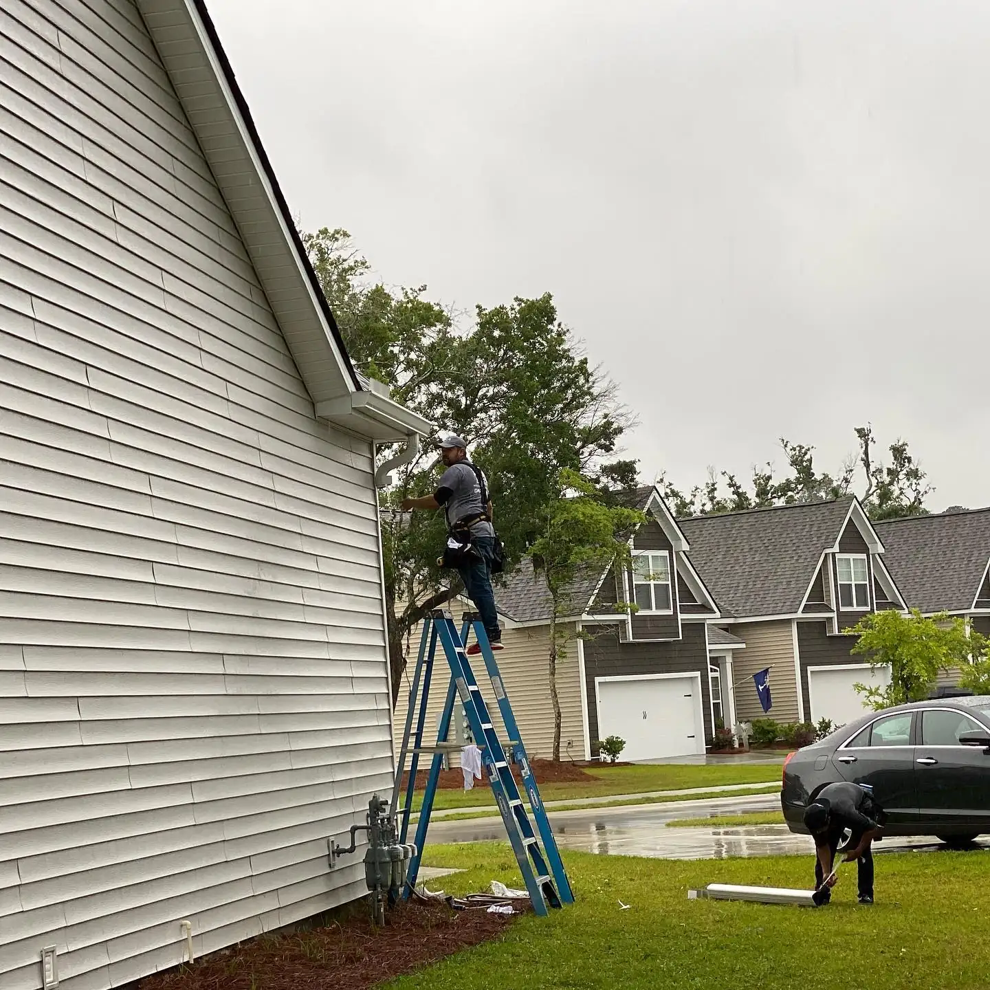 A&A crew member on a ladder working on the gutters of a gray two-story home. Gutter Installation in Bluffton, SC by A&A Island Services