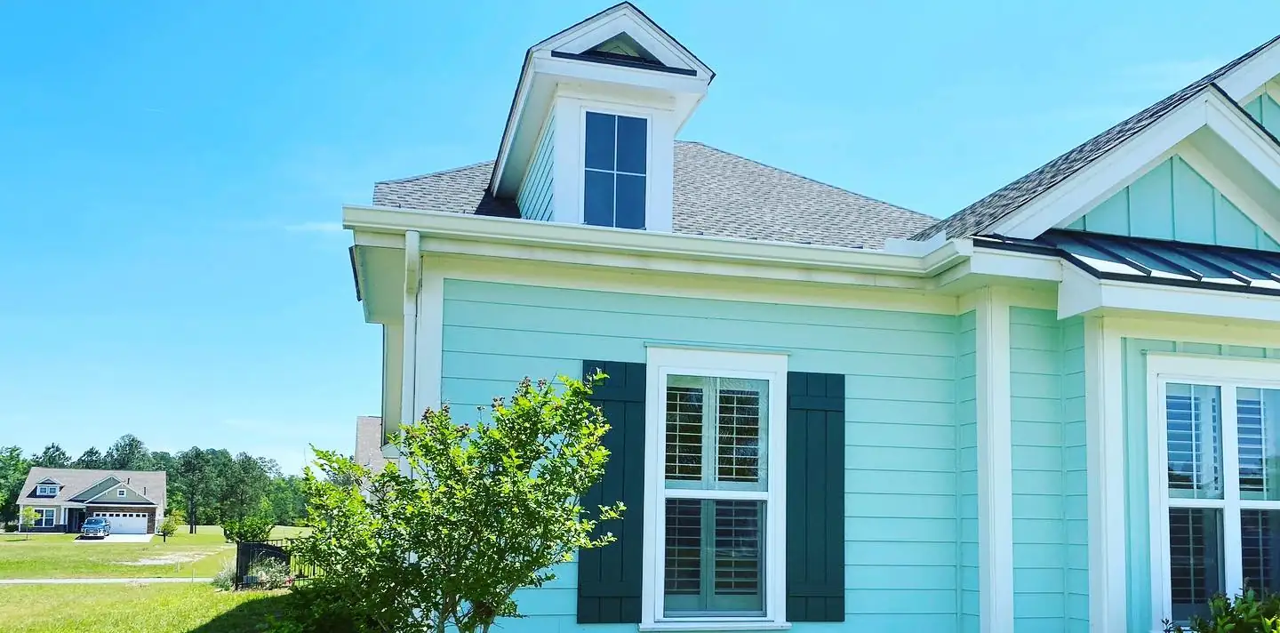 Dormer and roofline of a mint green home with white gutters and dark shutters. Gutter Installation in Bluffton, SC by A&A Island Services