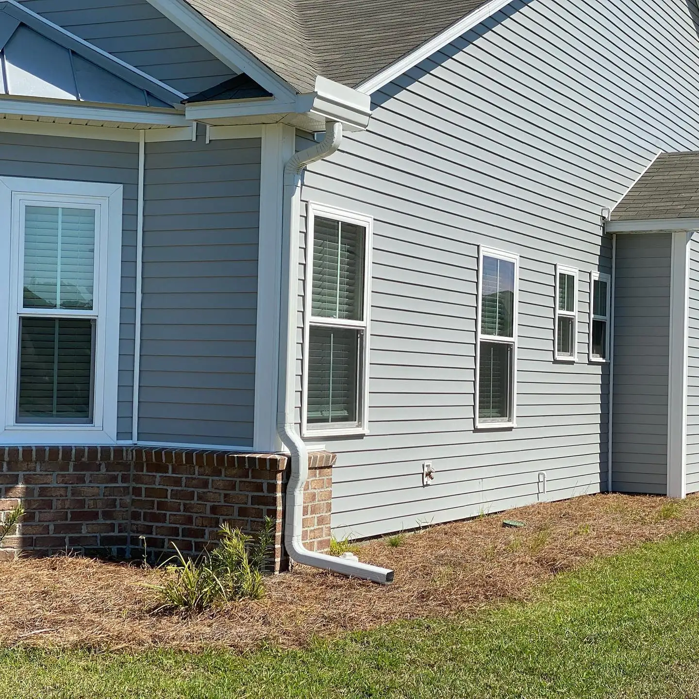 Corner of a gray home with a white downspout over a brick foundation. Gutter services in Sea Pines, SC by A&A Island Services