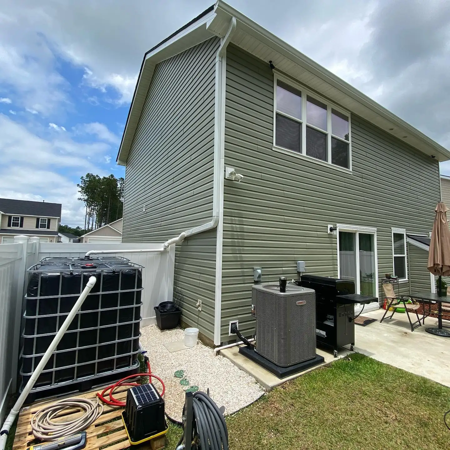 Downspout piped into a rainwater storage tank beside a two-story home with green siding. Downspouts in Bluffton, SC by A&A Island Services