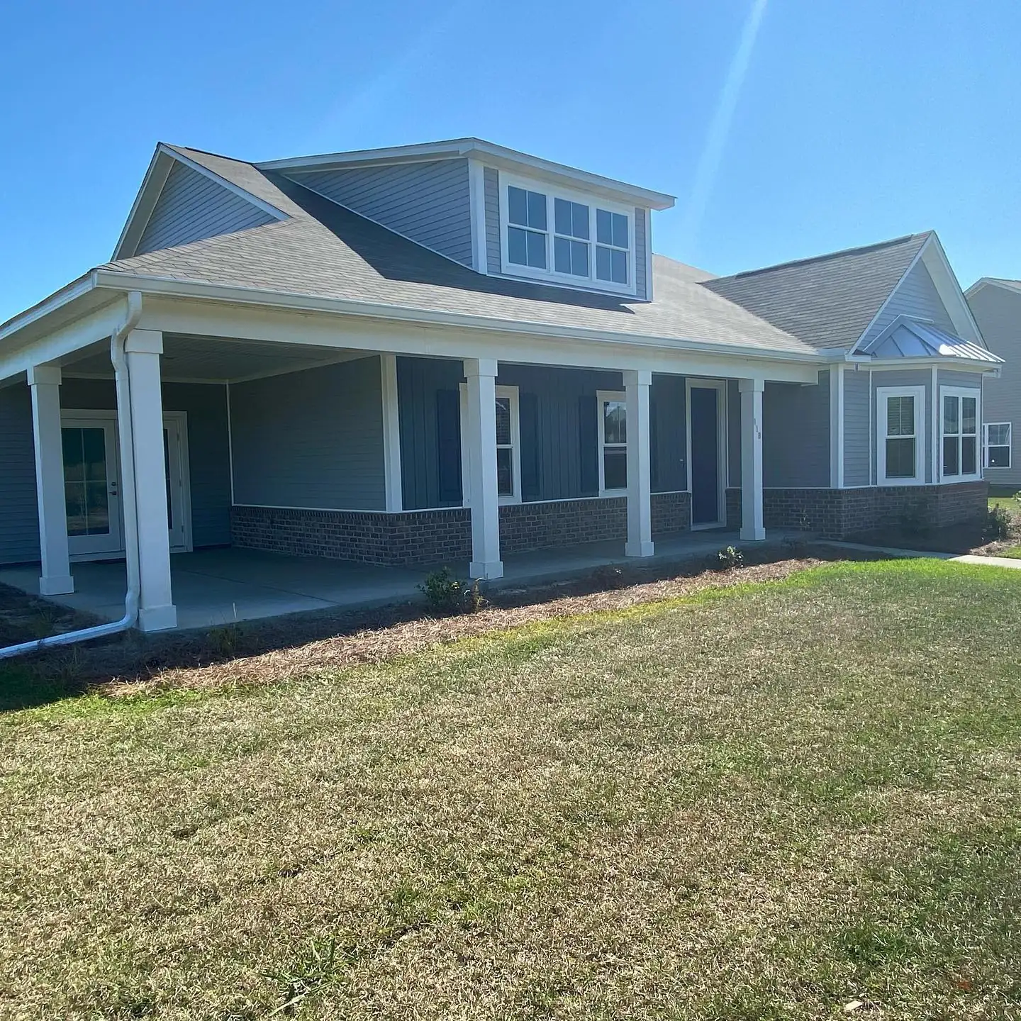 Gray home with a wide covered porch, a dormer and white gutters. Gutter cleaning and gutter installation in Bluffton, SC by A&A Island Services
