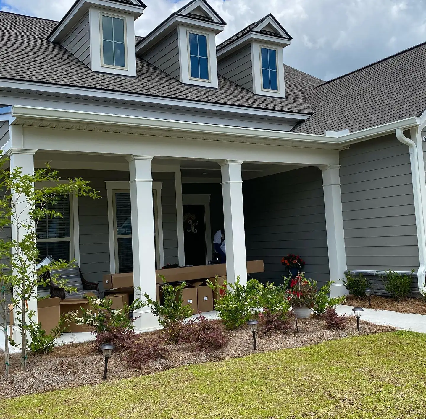 Gray home with three dormers, a white-columned front porch and white gutters. Gutter cleaning and gutter installation in Bluffton, SC by A&A Island Services