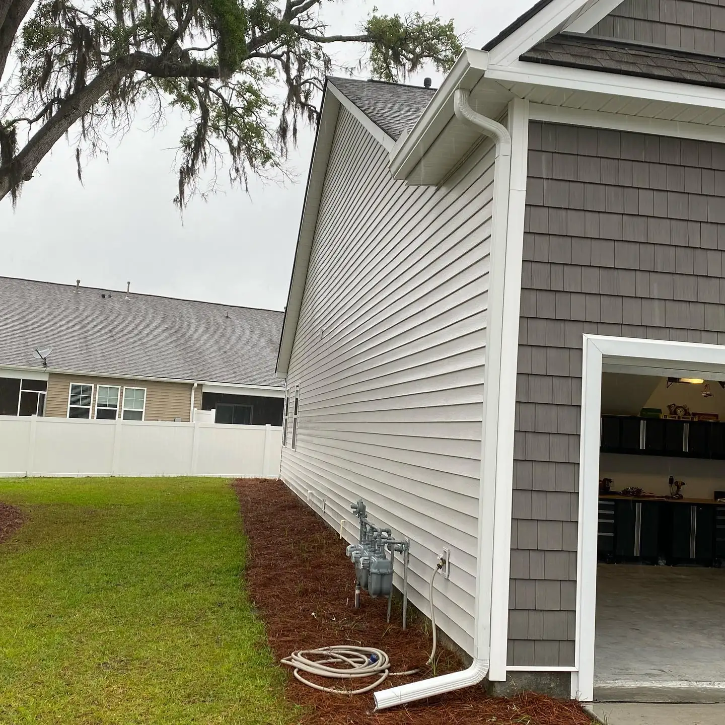 Side of a gray home with a white downspout next to an open garage. Gutter services in Sea Pines, SC by A&A Island Services