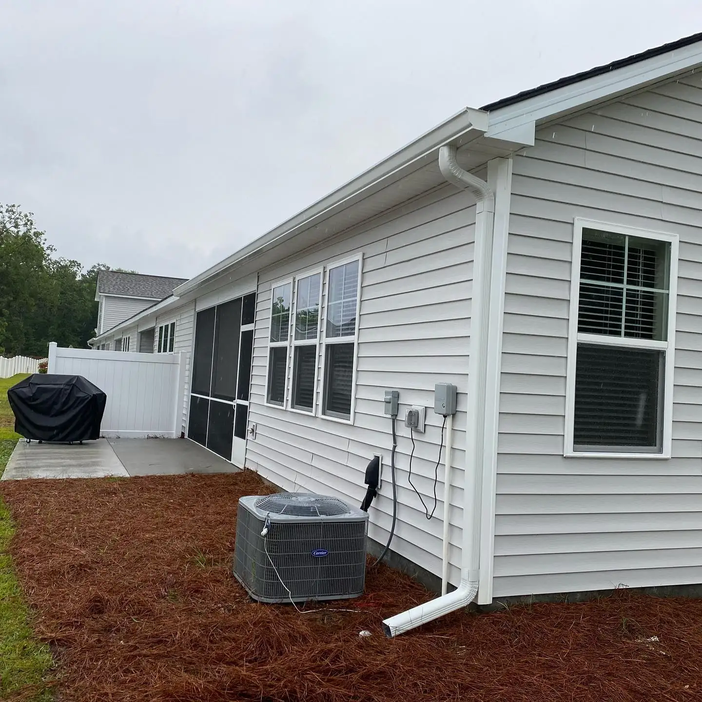 Side of a light gray home with white gutters and a downspout above fresh pine straw. Gutter Installation in Ridgeland, SC by A&A Island Services