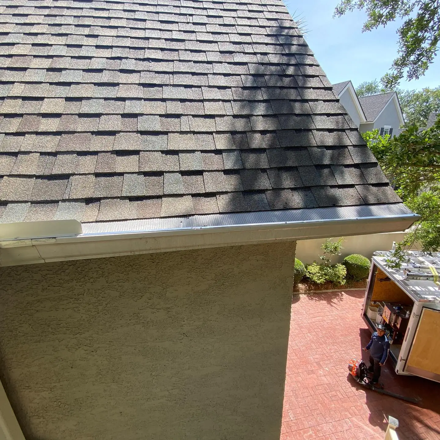 Gutter along a shingle roof edge above a stucco wall. Gutter Guards in Bluffton, SC by A&A Island Services