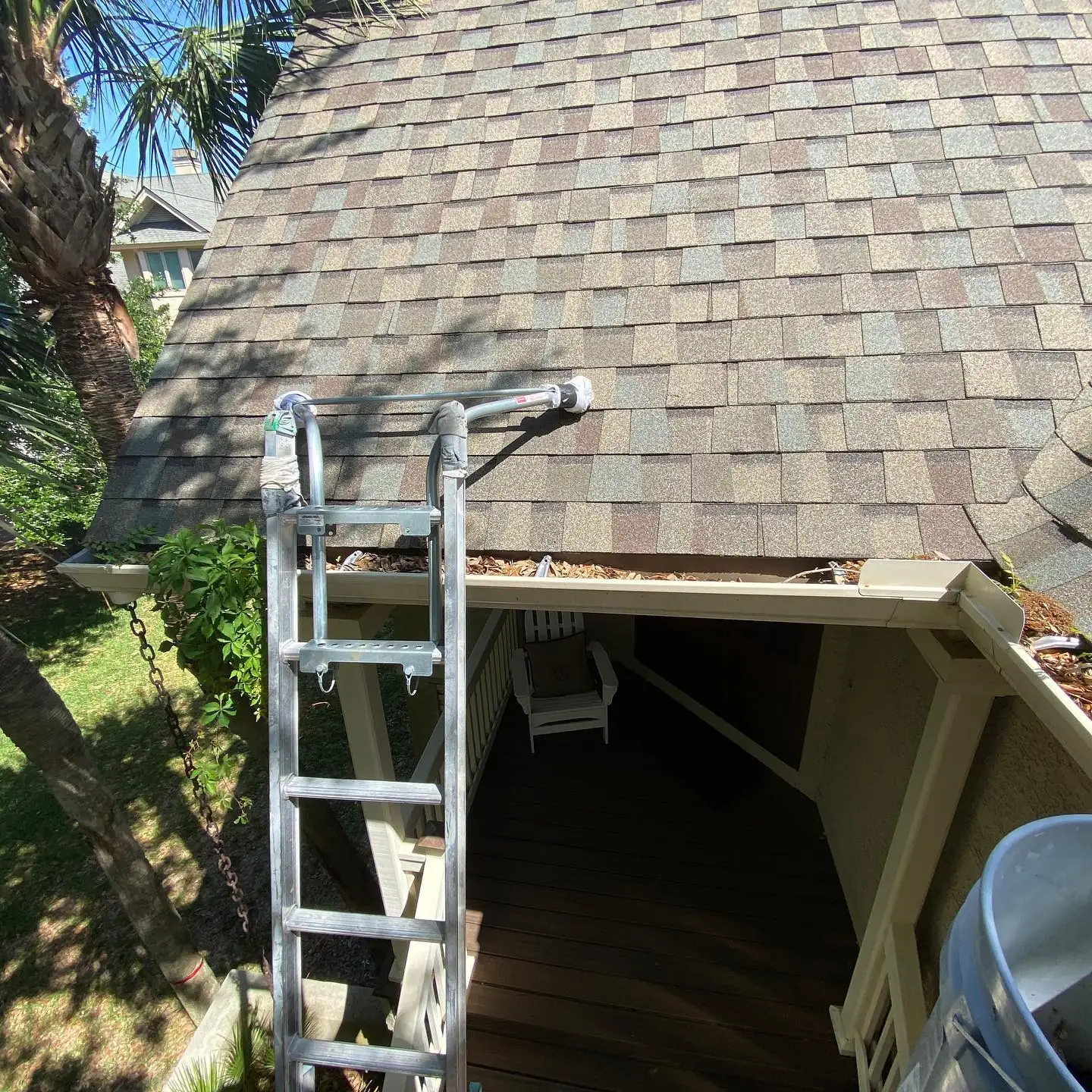 Gutter packed with pine needles and leaves below a shingle roof, with a ladder in place. Gutter Cleaning in Beaufort, SC by A&A Island Services