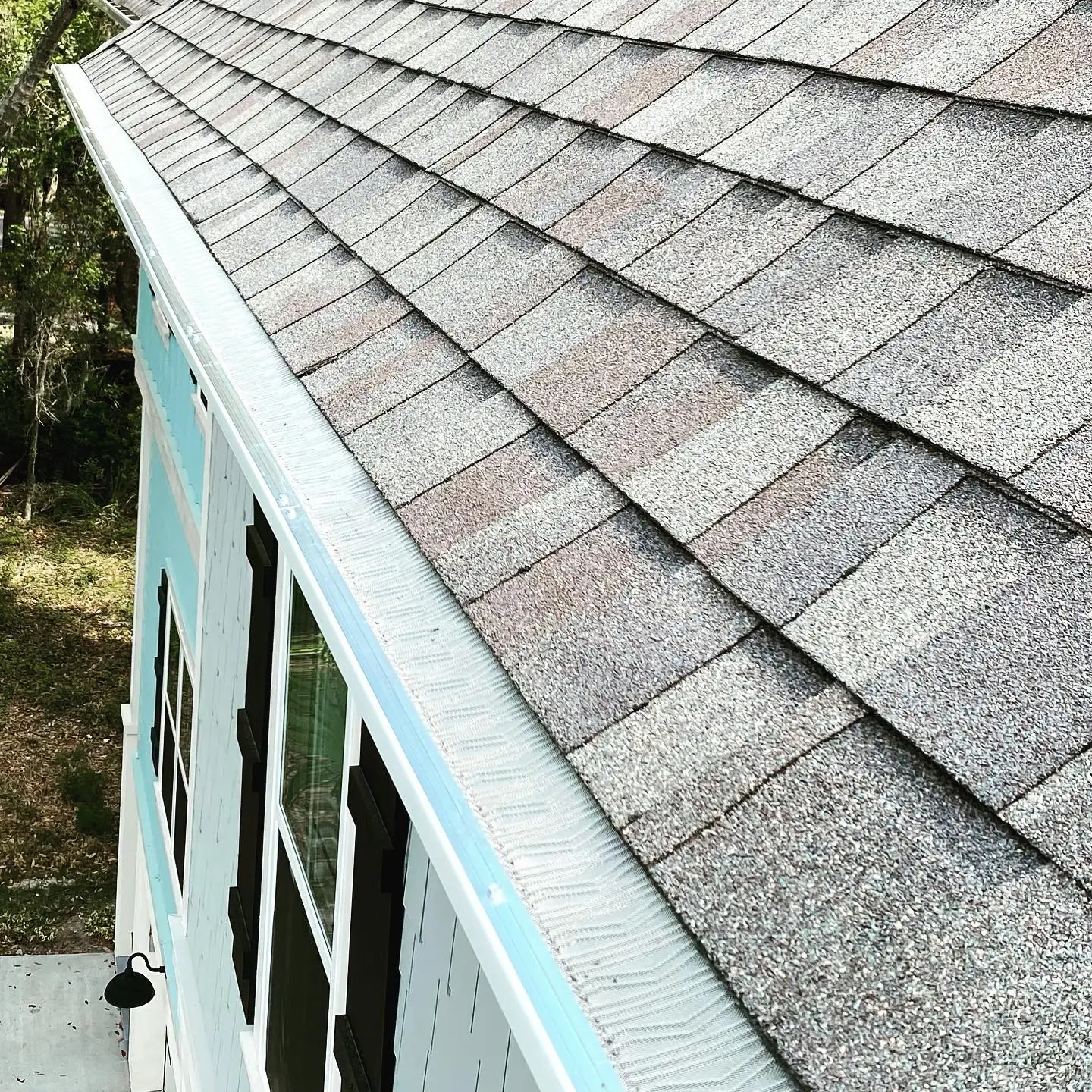 Gutter guard covering a gutter along the shingle roof edge of a light blue home. Gutter cleaning and gutter installation in Bluffton, SC by A&A Island Services