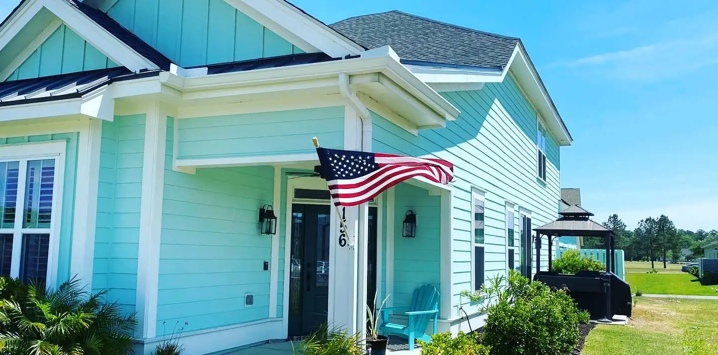 Mint green two-story home with white gutters, downspouts and an American flag at the front porch. Gutter services on Daufuskie Island, SC by A&A Island Services