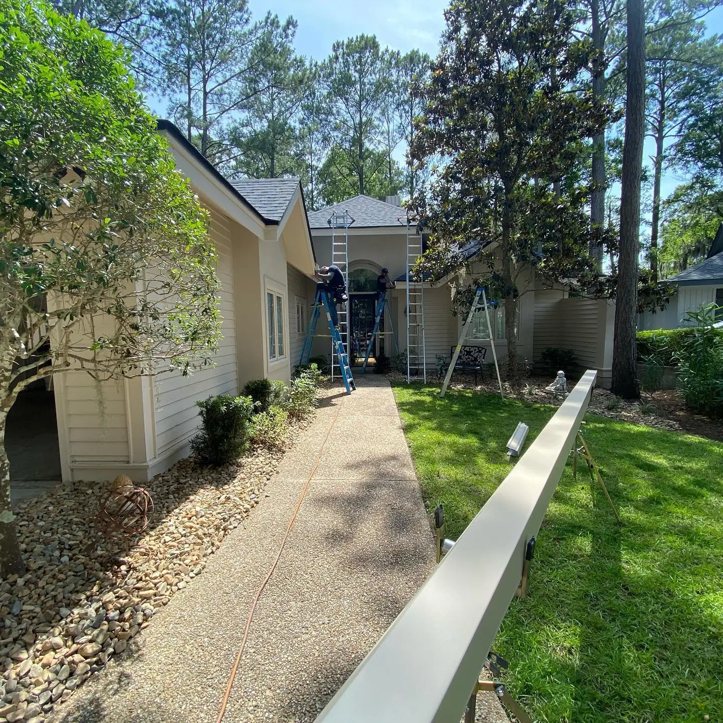 Long seamless gutter section laid along a walkway while the crew works on ladders. Gutter cleaning and gutter installation in Bluffton, SC by A&A Island Services