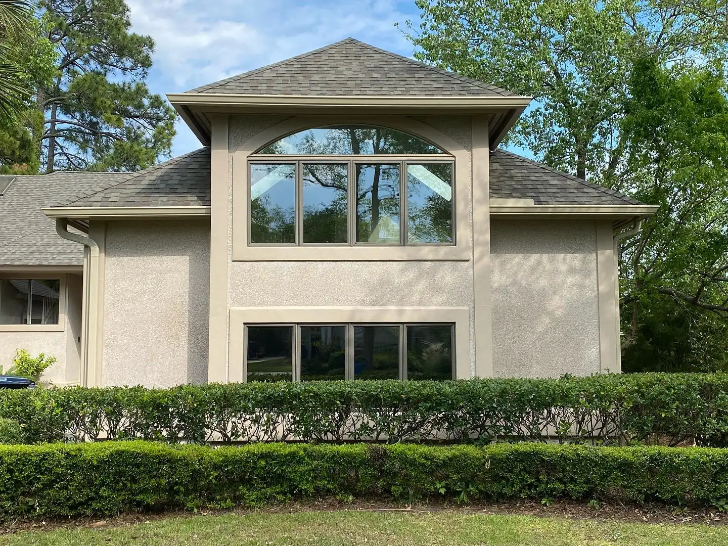 Two-story stucco home with an arched window and gutters behind a trimmed hedge. Gutter services in Sea Pines, SC by A&A Island Services