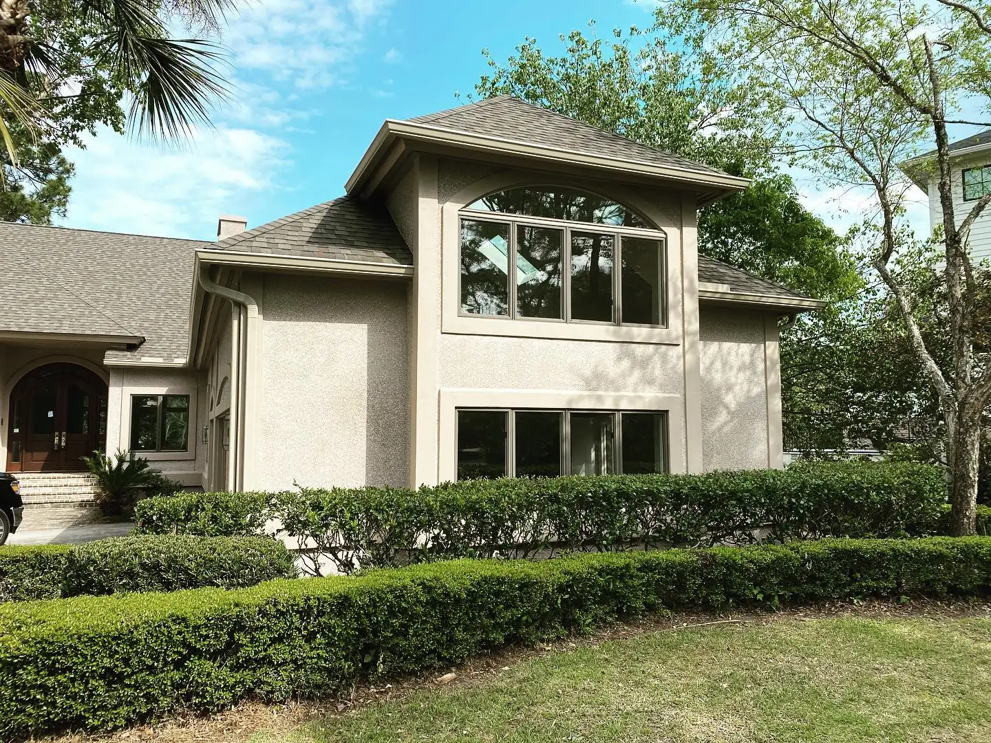 Two-story stucco home with gutters and a downspout behind a curved hedge. Gutter services in Hilton Head Plantation, SC by A&A Island Services