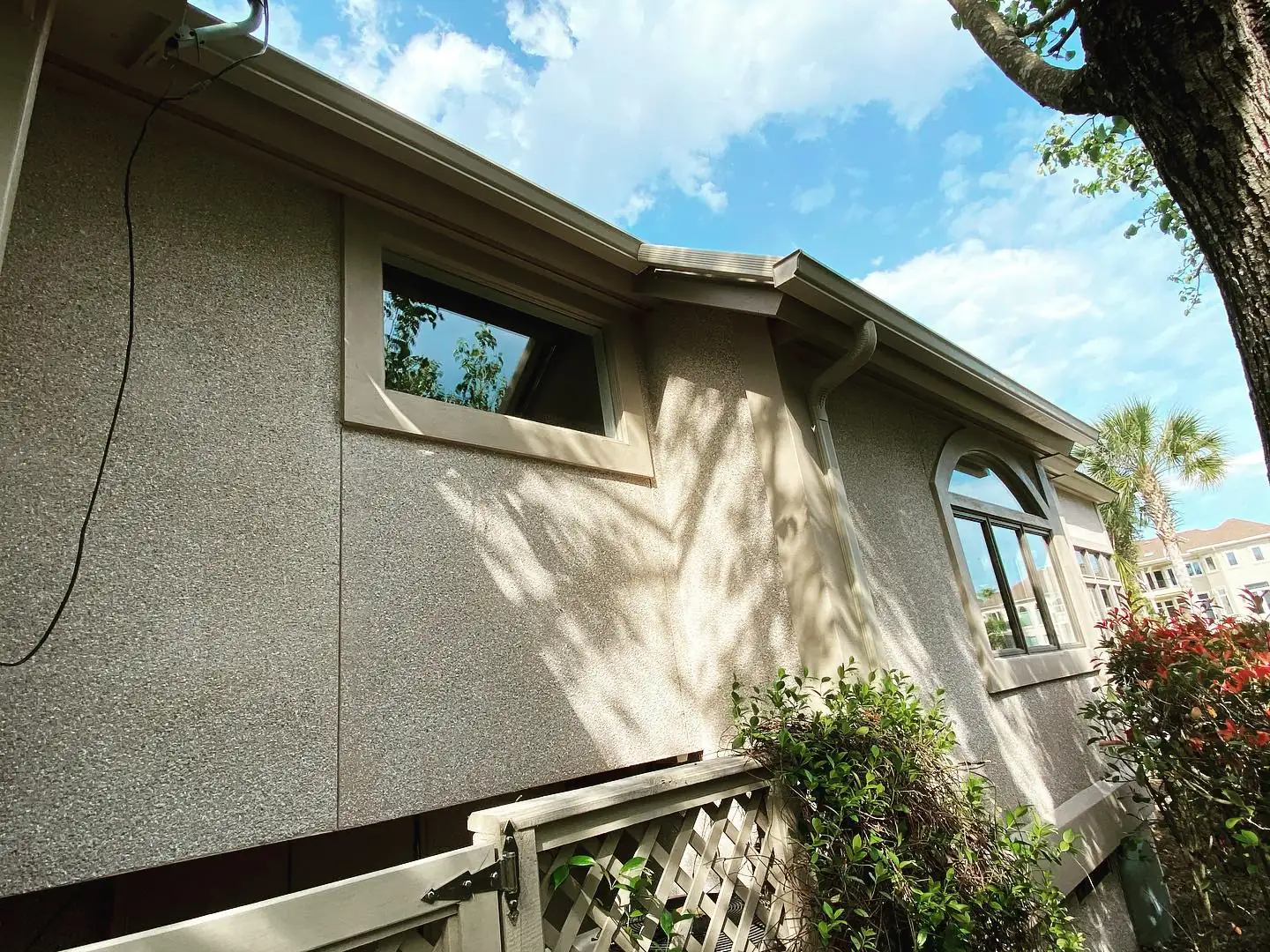 Stucco home with gutters along the roofline, seen from below under a shade tree. Gutter services in Hilton Head Plantation, SC by A&A Island Services