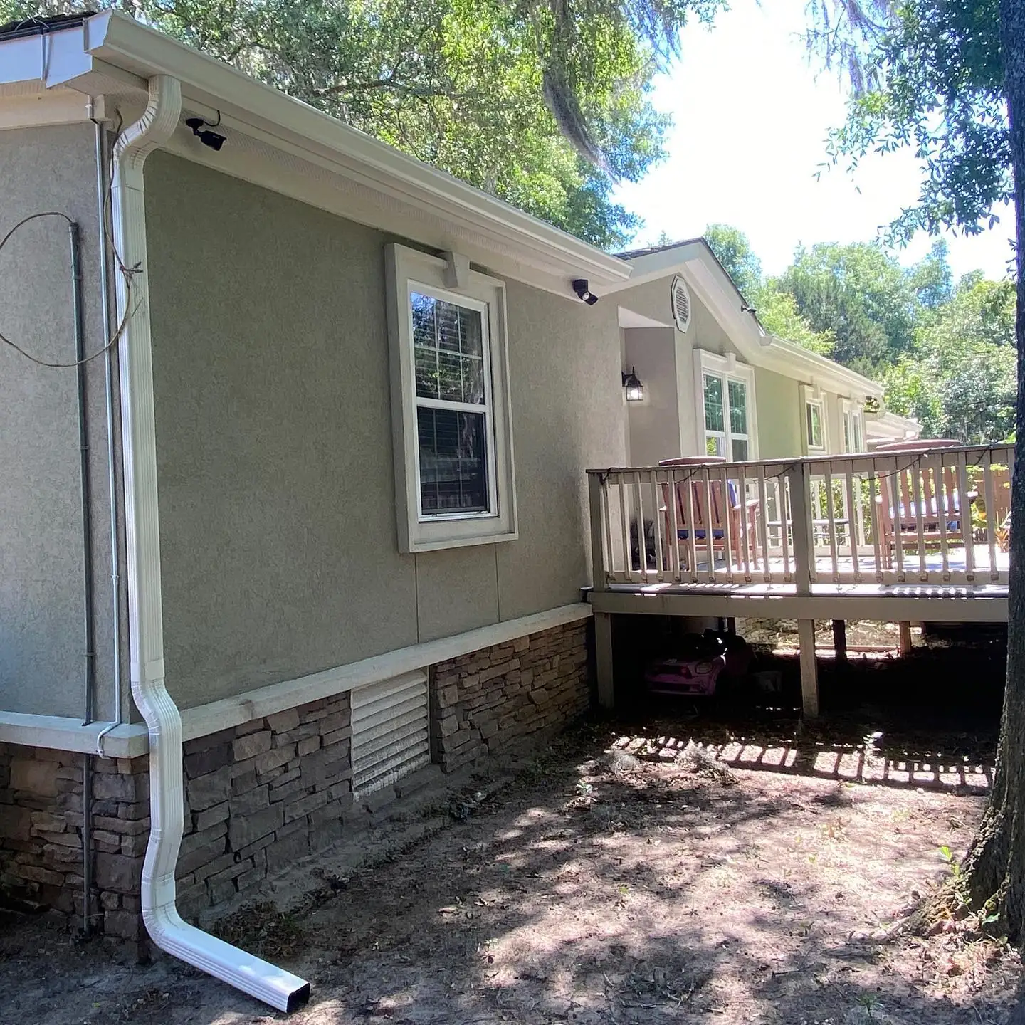 Stucco home with a white downspout running down to a stone base beside a raised deck. Gutter services in Pritchardville, SC by A&A Island Services