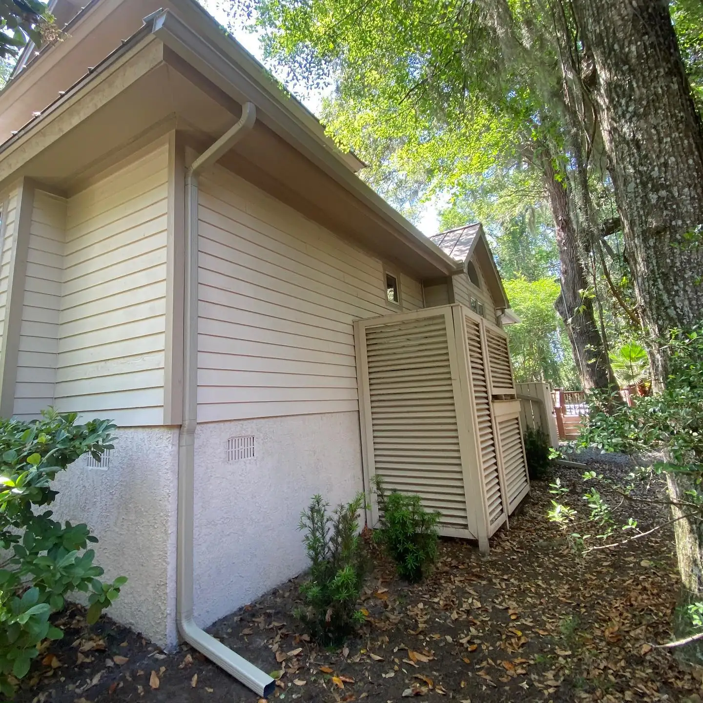 Tan home with a downspout tucked among trees and shrubs. Gutter services in Palmetto Dunes, SC by A&A Island Services