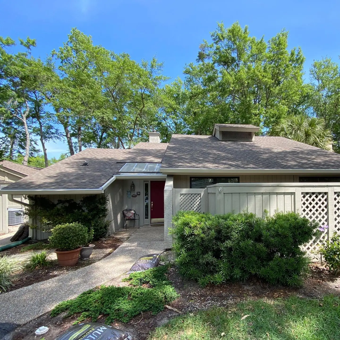 Single-story villa with a red door, lattice fence and gutters among tall trees. Gutter services in Pritchardville, SC by A&A Island Services